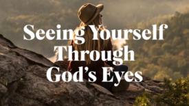 A person wearing a hat sits on a rocky overlook at sunset, gazing out over a forested valley. Text on the image reads: ‘Seeing Yourself Through God’s Eyes.’