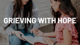 Two women sit together outdoors, holding hands as one of them opens a Bible on her lap. Text on the image reads: ‘Grieving with Hope.’